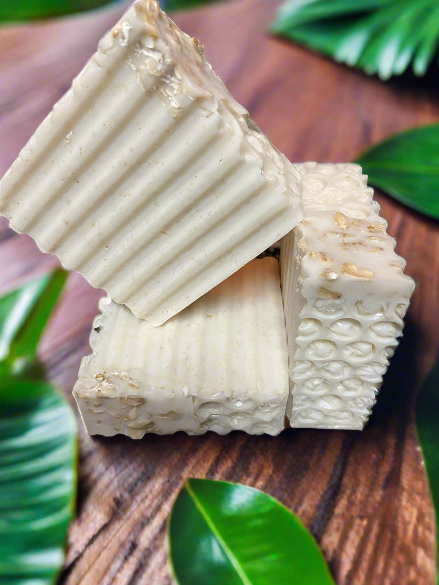 Three textured soap bars on a wooden surface with green leaves in the background